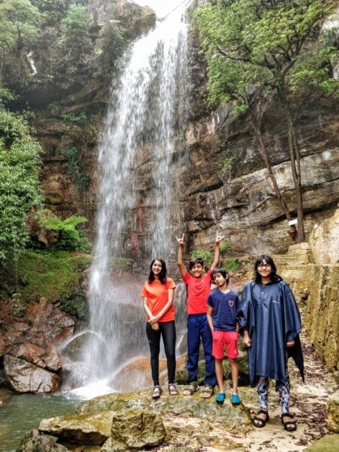 Children enjoying waterfall at Garden of Caves Meghalaya India.The Mesmerising hilly Meghalaya in the North East of India is Nature's well-kept secret. In this blog post, I have tried to cover 8 awesome places you must not miss to visit in Meghalaya including touristy destinations like Shillong and Cherrapunji and non-touristy places like Kongthong, this blog post has it all. So get your travel journals out to take notes and read on #lighttravelaction #shillong #cherrapunji #meghalaya #incredibleindia #offbeatindia #northeastindia #meghalayatravel