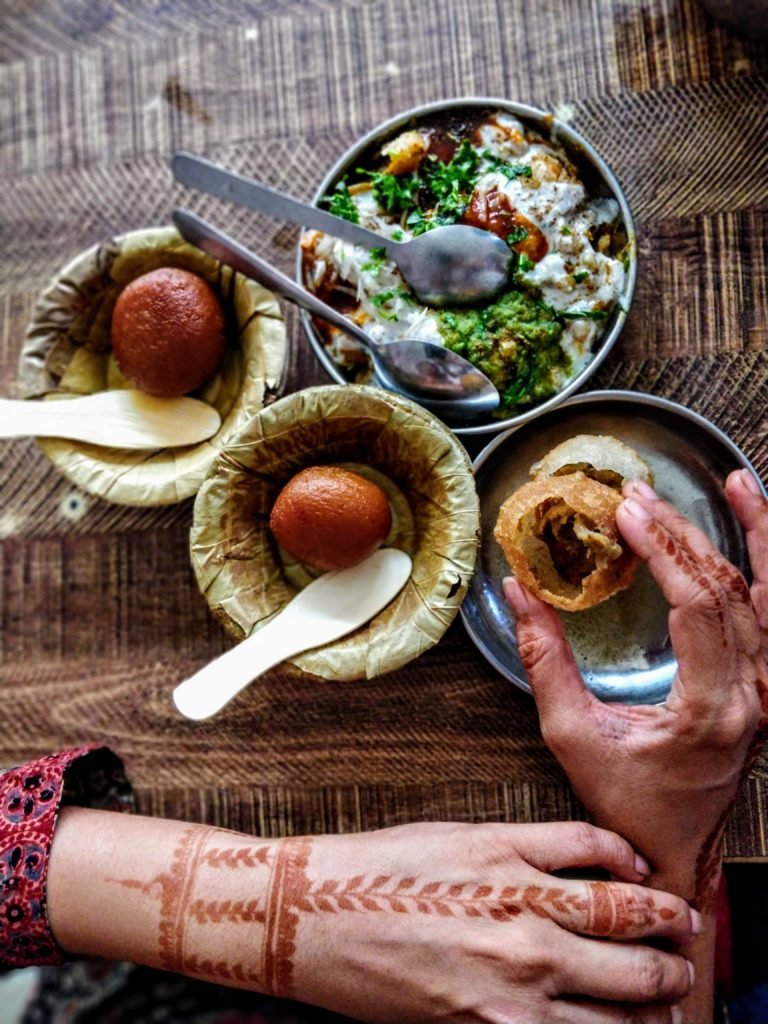 image of indian sweets gulab jamoon, pani puri, tamatar ki chaat and a henna tattooed hand