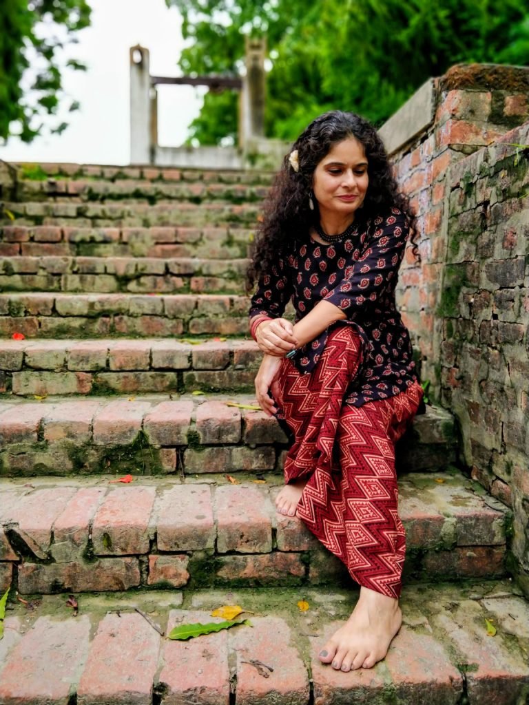 Woman sitting in maroon clothes on maroon steps which lead to the place where sant kabir was born