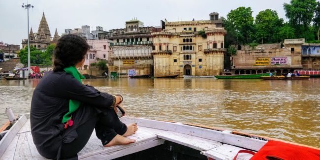 woman dressed in black salwar kurta sitting in a boat looking at the Varanasi ghat