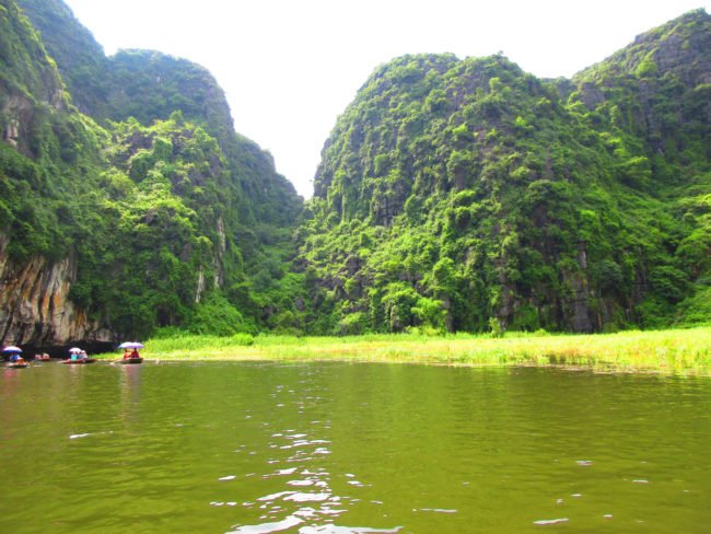 Boat ride in green coloured lake with green mountains around in ninh binh vietnam