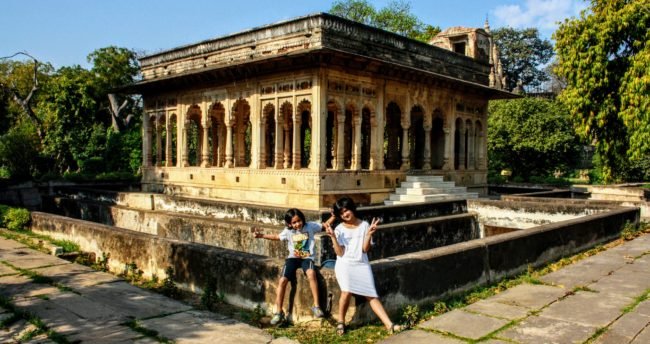 A girl and a boy sitting in front of the 17th century 36 arched doors pavilion in Neemrana's Deo Bagh Gwalior