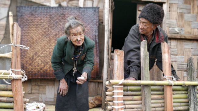 Apatani tribe old aged couple with tattooed face stand in front of their traditional house in Arunachal Pradesh, India