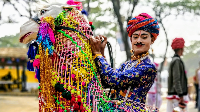 A man dressed in bright blue Rajasthani traditional dress and is riding an artificial cloth horse who is also decorated at the surajkund mela in Faridabad India